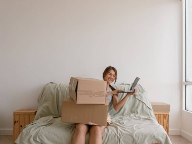 Taylandlı kadın karton kutular ve tablet tutarken yatakta gülümsüyor, rahat duruş, Asya kökenli