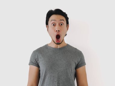 Asyalı adam tamamen şaşkın görünüyor, ağzı sonuna kadar açık, minimalist bir ortamda hem şok hem de heyecan gösteriyor.