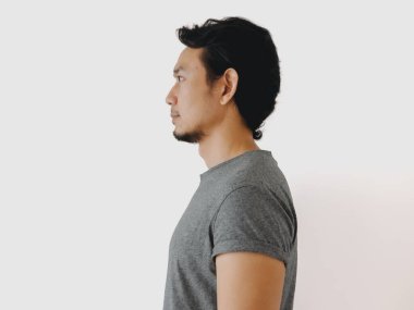 Bu resim, tarafsız bir arkaplana karşı gri tişört giyen bir adamın yan profilini gösteriyor.