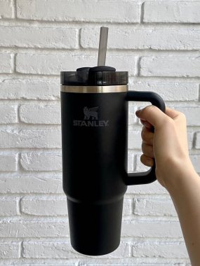 Barcelona, İspanya - 22 Eylül 2024: Hand Holding Black Stanley Quencher H2.0 FlowState Tumbler with Handle Against White Brick Wall. Yüksek kalite fotoğraf