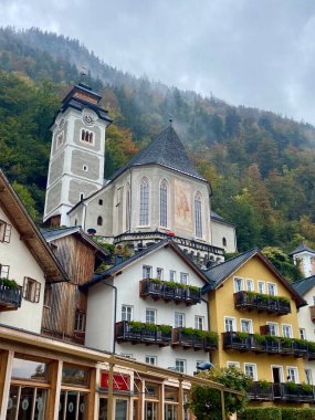 Hallstatt, Avusturya - 2 Ekim 2024: Renkli Evleri, Misty Dağları, Sonbahar Yeşillikleri olan Geleneksel Avusturya Köyü 'ndeki Kilise. Yüksek kalite fotoğraf