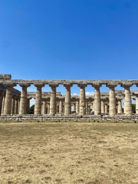 İtalya, Paestum 'daki Antik Yunan Tapınağı Harabeleri' nin Simetrik Çekimi, Parlak Mavi Gökyüzü ve Zamansız Güzellik tarafından çerçevelenmiştir. Yüksek kalite fotoğraf