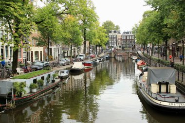 Amsterdam, The Netherlands - September 8 2018: Picturesque Amsterdam Canal with Traditional Houseboats, Waterfront Homes, and Scenic Reflections Surrounded by Trees and Bicycles. High quality photo clipart