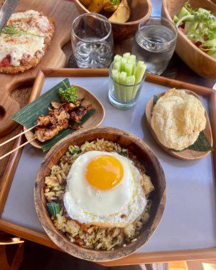 Geleneksel Bali Mutfak Tabağı 'nda kızarmış yumurta, tavuk şişi, taze sebze ve ahşap kaselerde çeşitli mezeler bulunan Nasi Goreng var. Yüksek kalite fotoğraf