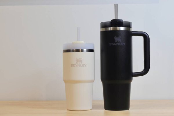 Two Stanley Cups, one Black and one Beige. Stylish Insulated Tumblers with Handles, Reusable Straws, and Stainless Steel Accents for Hot and Cold Beverages. High quality photo