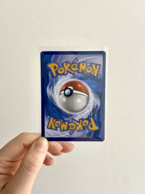 Barcelona, Spain - January 31 2024: Hand Holding a McDonald s Pokemon Trading Card in Protective Sleeve, Displaying Classic Blue Back Design with Poke Ball and Upside-Down Logo. Collectible TCG Item clipart