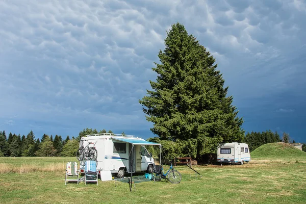 camping car and caravan near a firn tree on a campingsite in the french Auvergne under a cloudy sky in summer