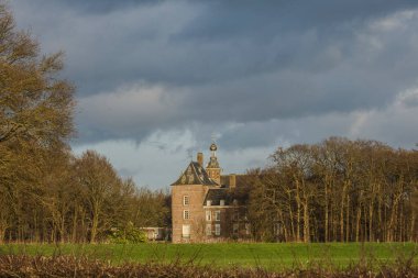sunbeams on a medieval castle of Laag Keppel under a cloudy, dark sky near river Oude IJssel on a winters day