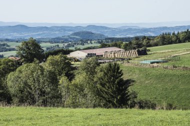 Fransız Bölgesi Auvergne tepelerindeki çayırlarda ahır ve saman balyaları olan bir çiftlik.