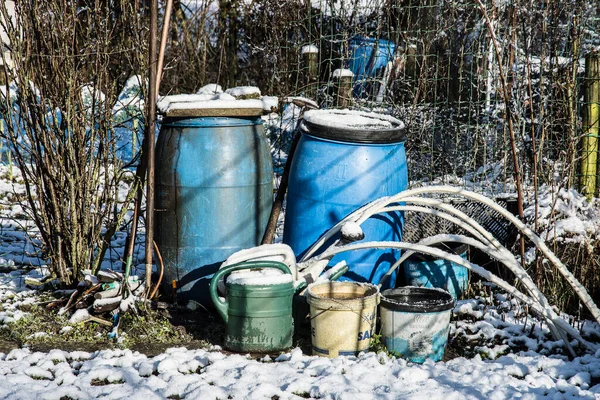 rain barrels and other garden tools covered with snow on a sunny day in the allotment garden