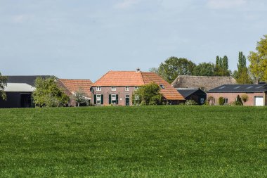 Ahırları ve çayırların arkasındaki ağaçları olan çiftlik evi.