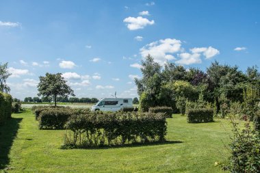 Kamp alanındaki beyaz bulutlu mavi gökyüzünün altındaki çitleri gören bir araba. 