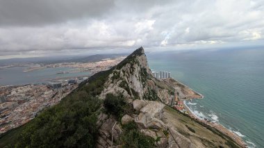 Cebelitarık Kayası 'ndan panoramik manzara engebeli bir uçurum, şehir manzarası ve bulutlu bir gökyüzünün altında Akdeniz. Doğal manzara ve şehir çevresi güzel bir şekilde birleşir..