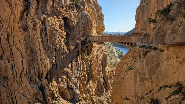 İspanya 'daki Caminito del Rey boyunca uzanan ünlü taş köprünün muhteşem manzarası. Köprü, yüksek uçurumlar ve parlak güneşli bir gökyüzünün altında engebeli kaya oluşumlarıyla çevrili dramatik bir vadiyi geçer..