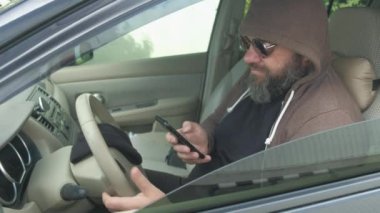 Kahverengi kapüşonlu ve siyah gözlüklü bir adam arabadaki telefonundan süzülüyor. Konuyu fark edince, fotoğraf çekmeye başladı. Görünmezlik, ajan, fotoğrafçı.