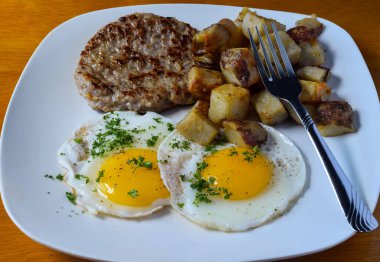 fried eggs top with parsley and served with sausage patty and home fries,