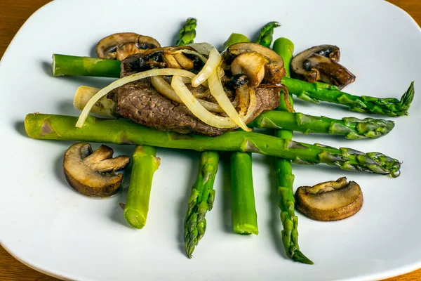 stock image an steak top with onions and mushrooms resting on asparagus