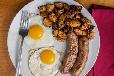 İki sahanda yumurta, yanında patates kızartması ve İtalyan sosisi.