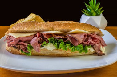 Kızarmış sığır eti, İsviçre peyniri ve patates cipsi ile servis edilir.