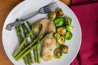 kızarmış brussel lahanası ve kuşkonmazla servis edilen tilapia.