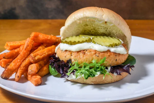 salmon burger  top with tarter sauce and pickles served with  sweet potato fries,