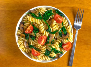 Sotelenmiş mantar ve domatesli ıspanak içeren rotini makarna salatası., 