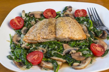 Fırında somon balığı sotelenmiş ıspanak ve mantarla servis edilir.