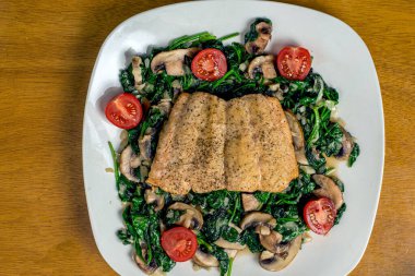 Fırında somon balığı sotelenmiş ıspanak ve mantarla servis edilir.