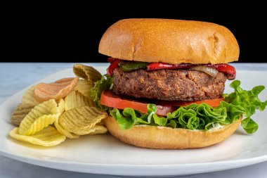 Sebze cipsiyle servis edilen sotelenmiş soğanlı ve biberli hamburger.