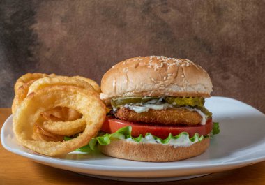 soğan halkalarının yanında servis edilen susamlı ekmeğin üzerinde balık fileto sandviç.