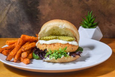 Tartar soslu somon burger üstü ve patates kızartmasıyla servis edilen turşu.,