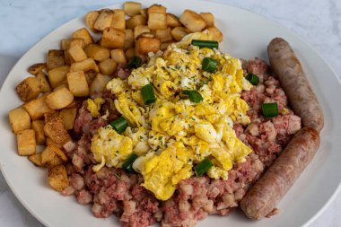 Çırpılmış yumurta üstü maydanozlu ve yeşil soğanlı mısır sığır eti ve patates kızartması.