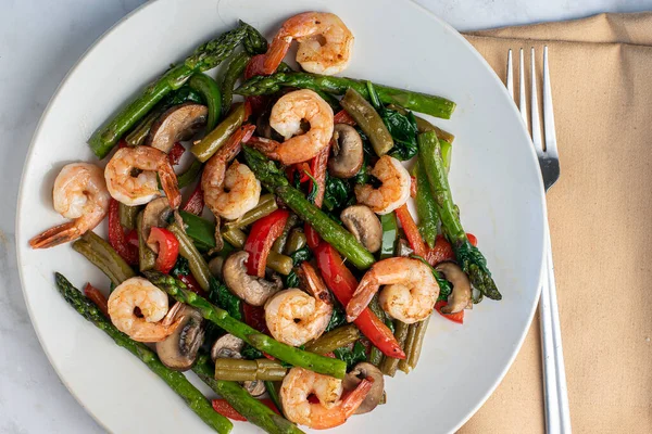 Kuşkonmaz fasulye ve mantarla servis edilen sotelenmiş karides., 