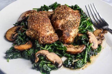 Sotelenmiş ıspanak ve mantarla servis edilen daha az tavuk butları..