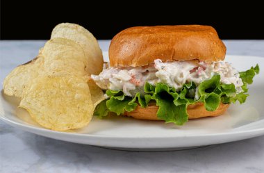 Çörekli yengeç salatası patates cipsiyle servis ediliyor.