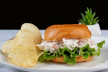 Çörekli yengeç salatası patates cipsiyle servis ediliyor.