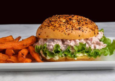 Tatlı patates kızartmasıyla servis edilen brioche ekmeğinin üzerine jambon salatası.