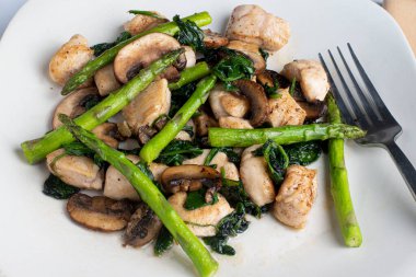 Sotelenmiş kuşkonmaz, ıspanak ve mantarla servis edilen tavuk ısırıkları.,