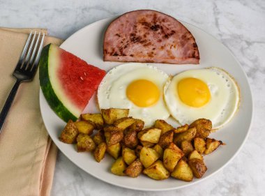 iki sahanda yumurta, patates kızartması, jambon ve bir dilim karpuz.