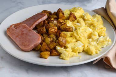 Yağda yumurta, patates kızartması ve kızarmış konserve jambonla servis ediliyor.