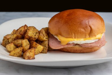  Kızarmış jambonlu yumurta, yanında patates kızartması ve brioche rulosuyla servis ediliyor., 