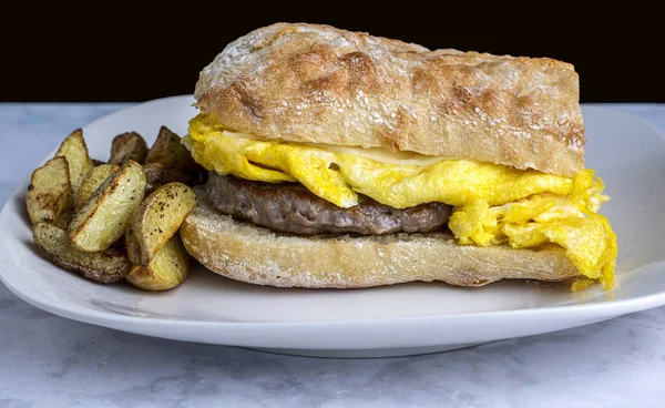 Ciabatta ekmeğinin üstünde yumurta ve sosisli börek ve yanında patates kızartması.