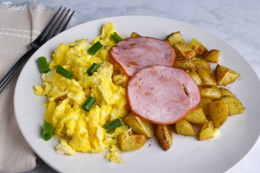 Kanada pastırması çırpılmış yumurta ve kızarmış patates ile servis edilen yeşil soğan üzerinde dinleniyor.