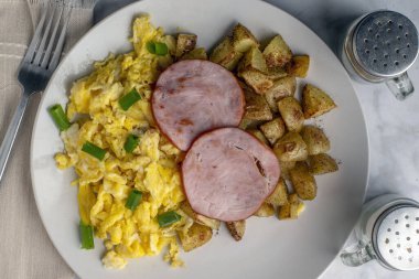 Çırpılmış yumurta, soğan ve Kanada pastırması ile servis edilen patates kızartması.,