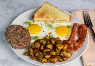 İki sahanda yumurta maydanozlu ve yeşil soğanlı sosis, pastırma ve patates kızartması.