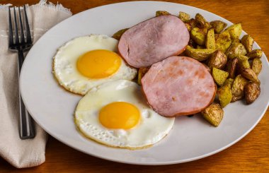 Kızarmış yumurta ve patates kızartması Kanada pastırması ile servis ediliyor., 
