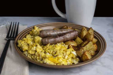 Üzerine biber ve baharatla çırpılmış yumurta ve yanında patates kızartması ve kahvaltı sosisi., 