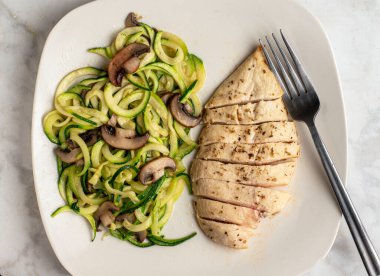 Dilimlenmiş tavuk göğsü. Kabaklı erişteyle servis ediliyor. Üstü mantarlı.,