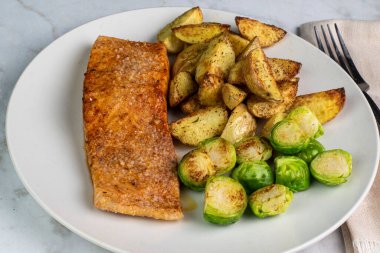 Patates dilimleri ve kızarmış brussel filizleriyle servis edilen baharatlı somon balığı.