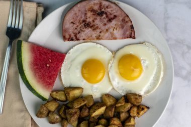 iki sahanda yumurta, patates kızartması, jambon ve bir dilim karpuz.